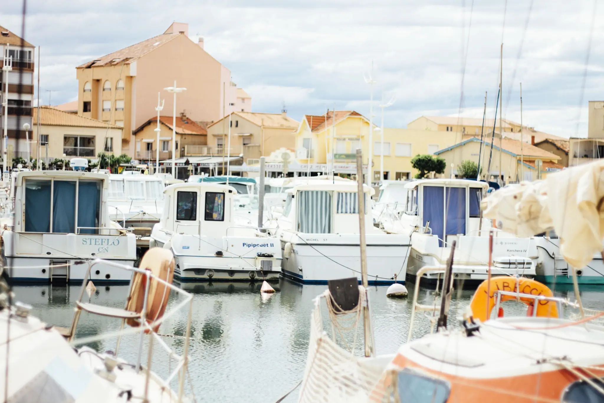 A marina with various boats docked, buildings in the background, and a clear sky.