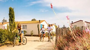 A residential area with houses, a pathway, and a person on a bicycle. - KLASSIK 2-Bedroom Mobile Home "DIMANCHE" - No Air Conditioning - Sleeps 5 (SERIGNAN)