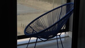 A balcony with a blue wire chair, a view of buildings in the background. - cozy 2-bedroom apartment with sea view in Al Khobar (Al Khobar)