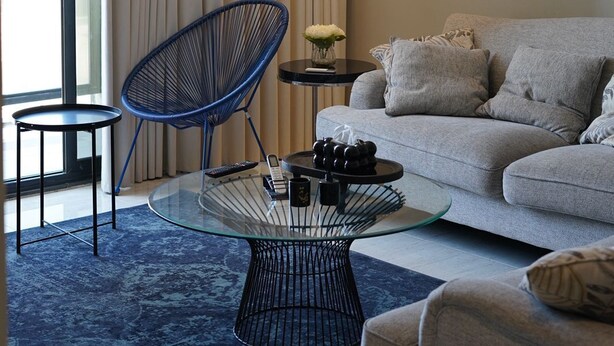 A modern living room with a grey sofa, a blue chair, a glass coffee table, and a unique spherical chandelier. - cozy 2-bedroom apartment with sea view in Al Khobar (Al Khobar)