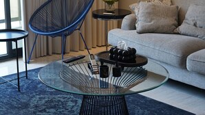 A modern living room with a round glass coffee table, a blue wire chair, a grey sofa, and a small side table with a vase of flowers. - cozy 2-bedroom apartment with sea view in Al Khobar (Al Khobar)