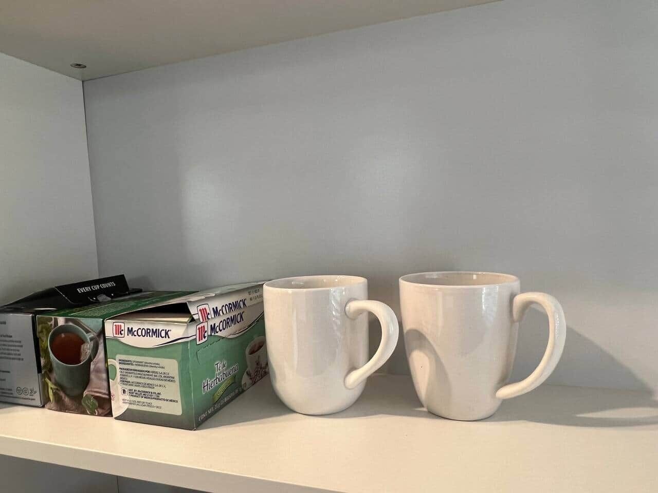 Una caixa de te aromatitzat amb herbes McCormick i dues tasses de ceràmica blanca sobre una estant blanca.
