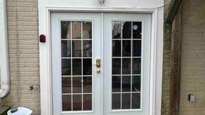 A white double door with a brass handle, a small window above it, and a brick wall.