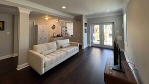A spacious living room with a large sofa, a television, and a kitchen area in the background.
