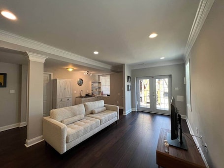 A spacious living room with a large sofa, a television, and a kitchen area in the background.