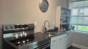 A kitchen with a stainless steel stove, a sink, a clock, and a window with blinds.