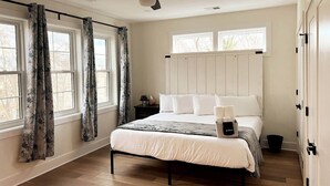 Un dormitorio con cama, mesita de noche, ventilador de techo y ventana con cortinas.