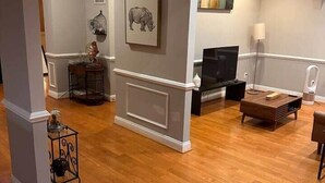 Een ruime woonkamer met houten vloeren, een televisie en een open haard.