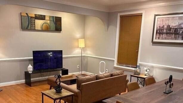 Een moderne woonkamer met een bank, een salontafel, een televisie en een eettafel met stoelen.