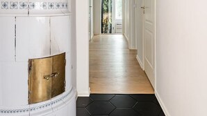 Un couloir avec un mur recouvert de carreaux blancs, un sol noir à motifs hexagonaux et une porte en laiton.