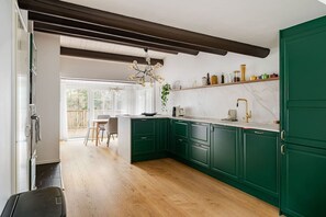 Une cuisine avec des meubles de couleur verte, un plan de travail en marbre et un luminaire suspendu.