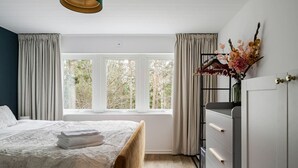 Une chambre à coucher avec un lit, une commode, une fenêtre avec des rideaux et une plante suspendue.