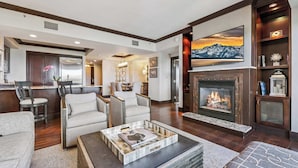 A modern living room with a fireplace, comfortable seating, a kitchen area, and a large TV mounted above the fireplace. - Northstar Resort Mid-Mountain Ski in/Ski in/Ski out 3 bedroom condo (Truckee)
