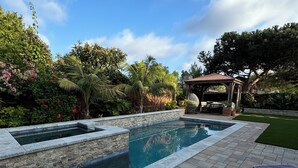 A swimming pool with a stone border, surrounded by a patio area with lounge chairs and a pergola.