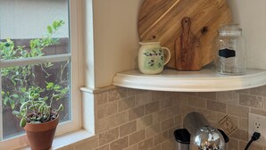 A kitchen with a window, a Nespresso coffee machine, a wooden cutting board, a ceramic pitcher, and a vase with birds.
