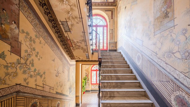 Una imponente escalera adornada con decoraciones en las paredes y una puerta roja en la parte superior.