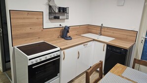 A compact kitchen with a built-in stove, oven, and dishwasher. A small sink and a coffee maker are also visible. - Apparently (Naintré)