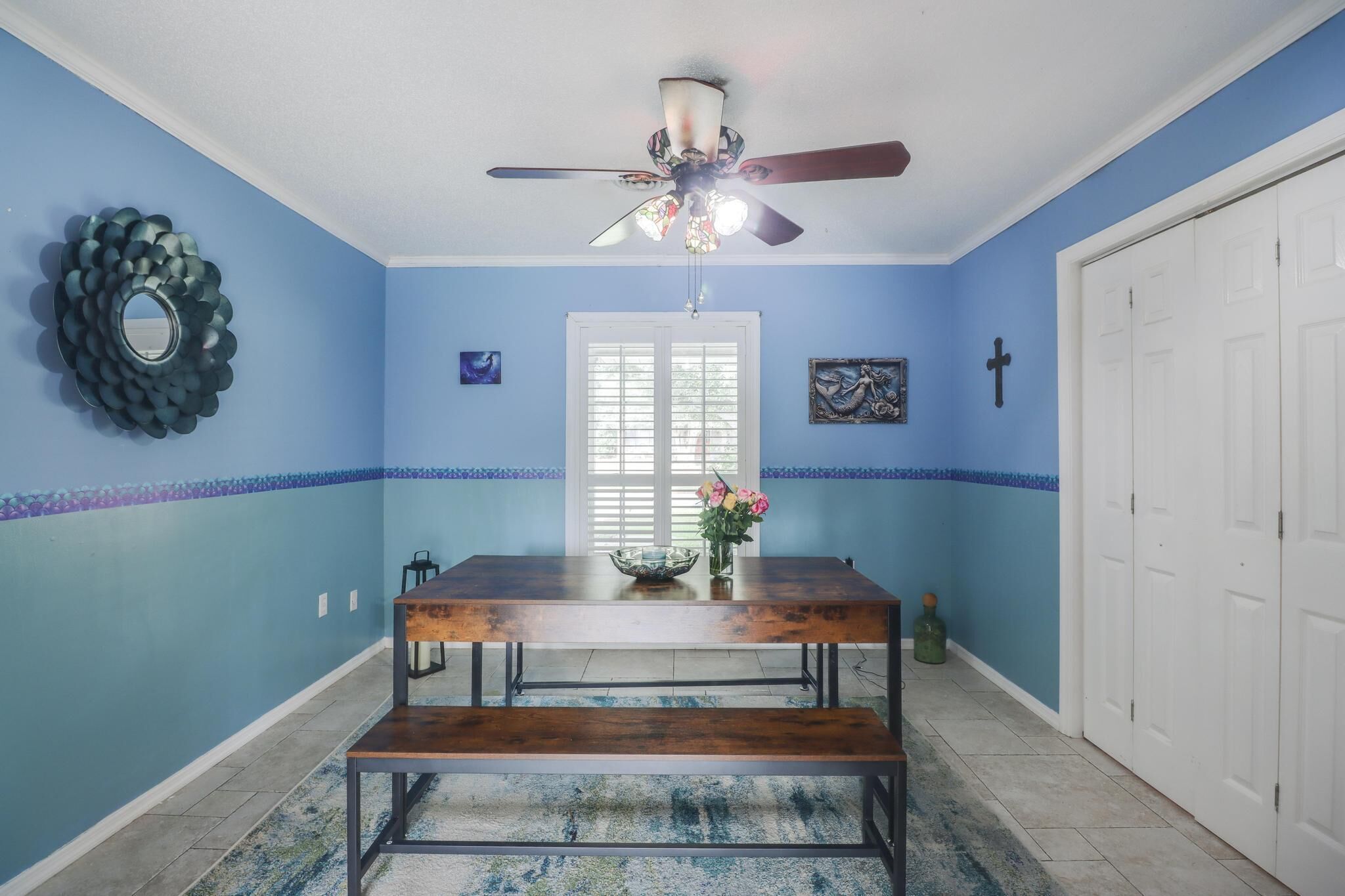 Un espace repas comprenant une table en bois, un banc, un ventilateur de plafond et des éléments décoratifs sur les murs.