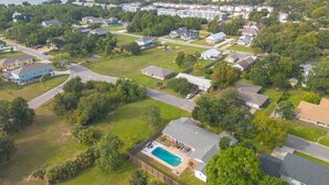 Vue aérienne d’un quartier résidentiel avec des maisons, une piscine et une plage en arrière-plan.