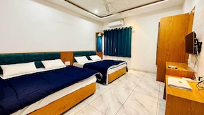 A hotel room with two beds, a wooden wardrobe, a desk, and a ceiling fan.