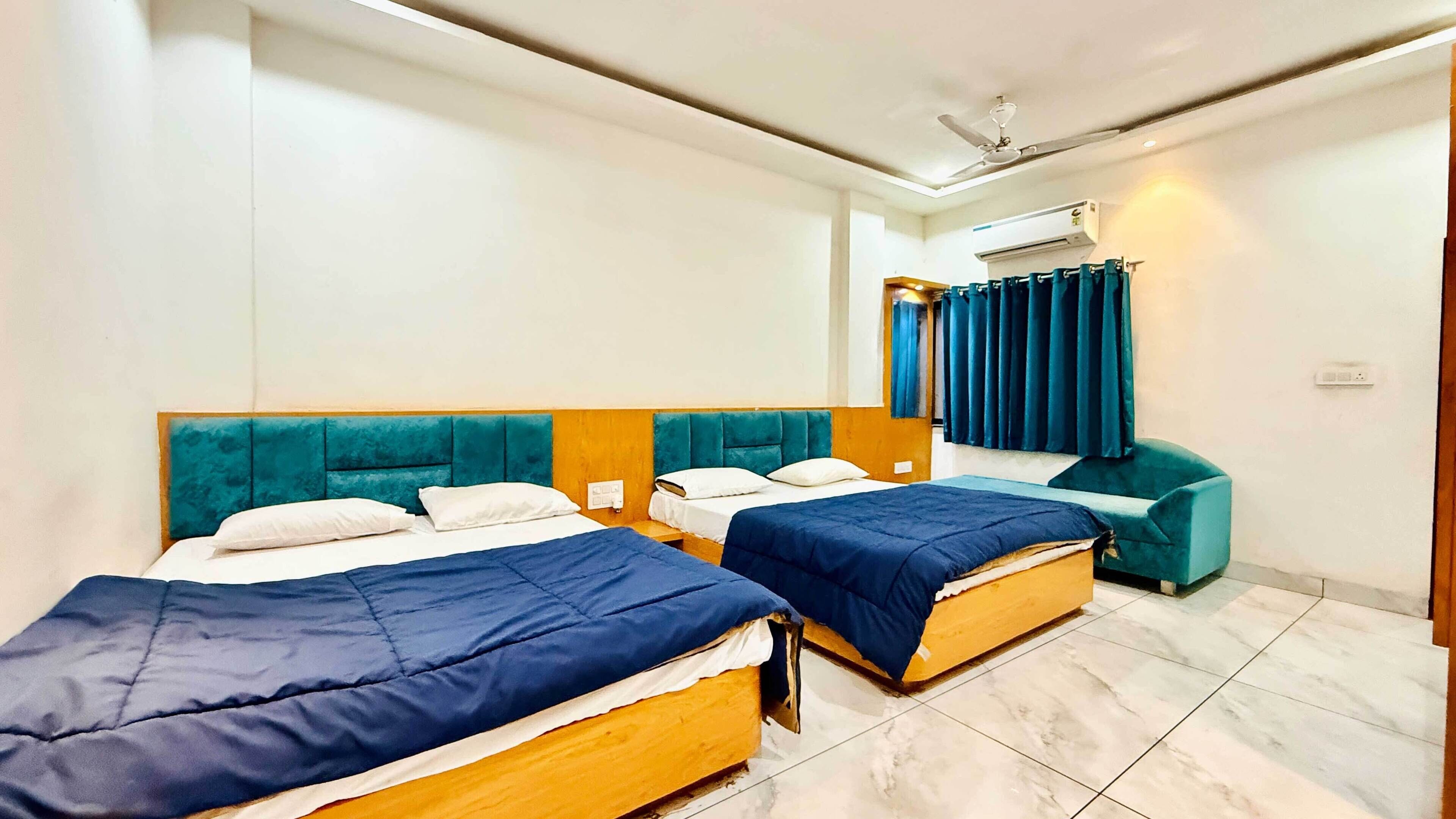 A hotel room with two beds, a ceiling fan, an air conditioning unit, and a window with curtains.