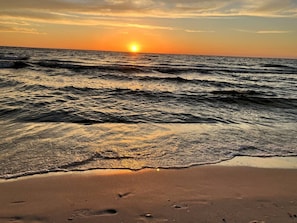 Une plage avec des vagues, un soleil visible et un ciel dégagé.