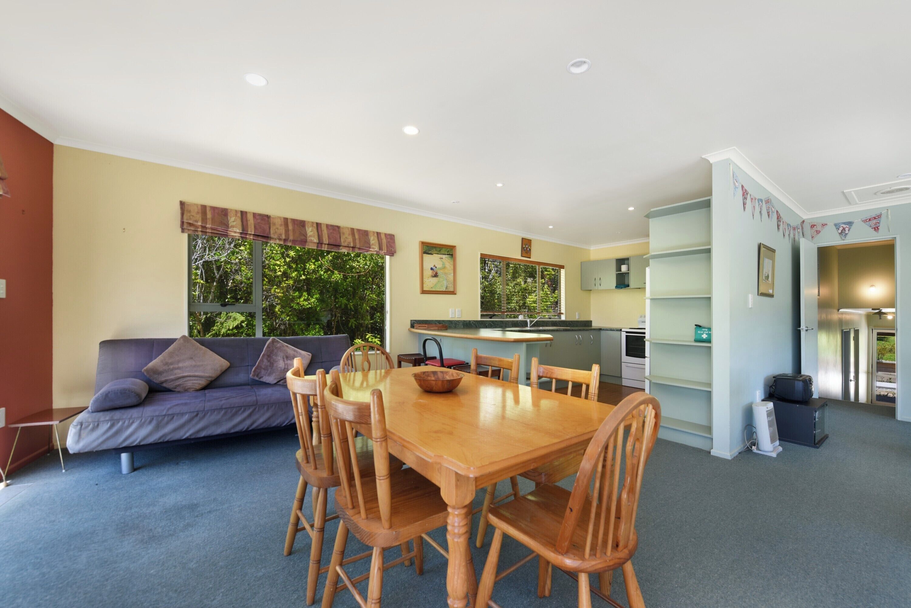 A living room with a sofa, wooden dining table, and chairs. There is a kitchen area with a counter and cabinets.