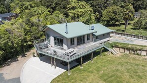 A modern house with a large deck, a covered outdoor area, and a view of surrounding greenery. - Kereru Retreat at Moetapu Bay (Moetapu Bay)