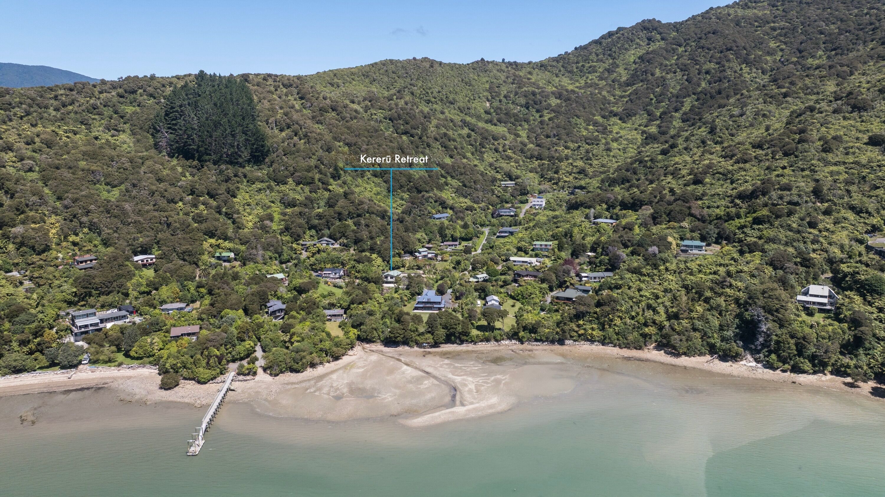 Ein Küstenurlaubsort mit mehreren Häusern, umgeben von dichtem Wald, einem Sandstrand und einer ruhigen Bucht.