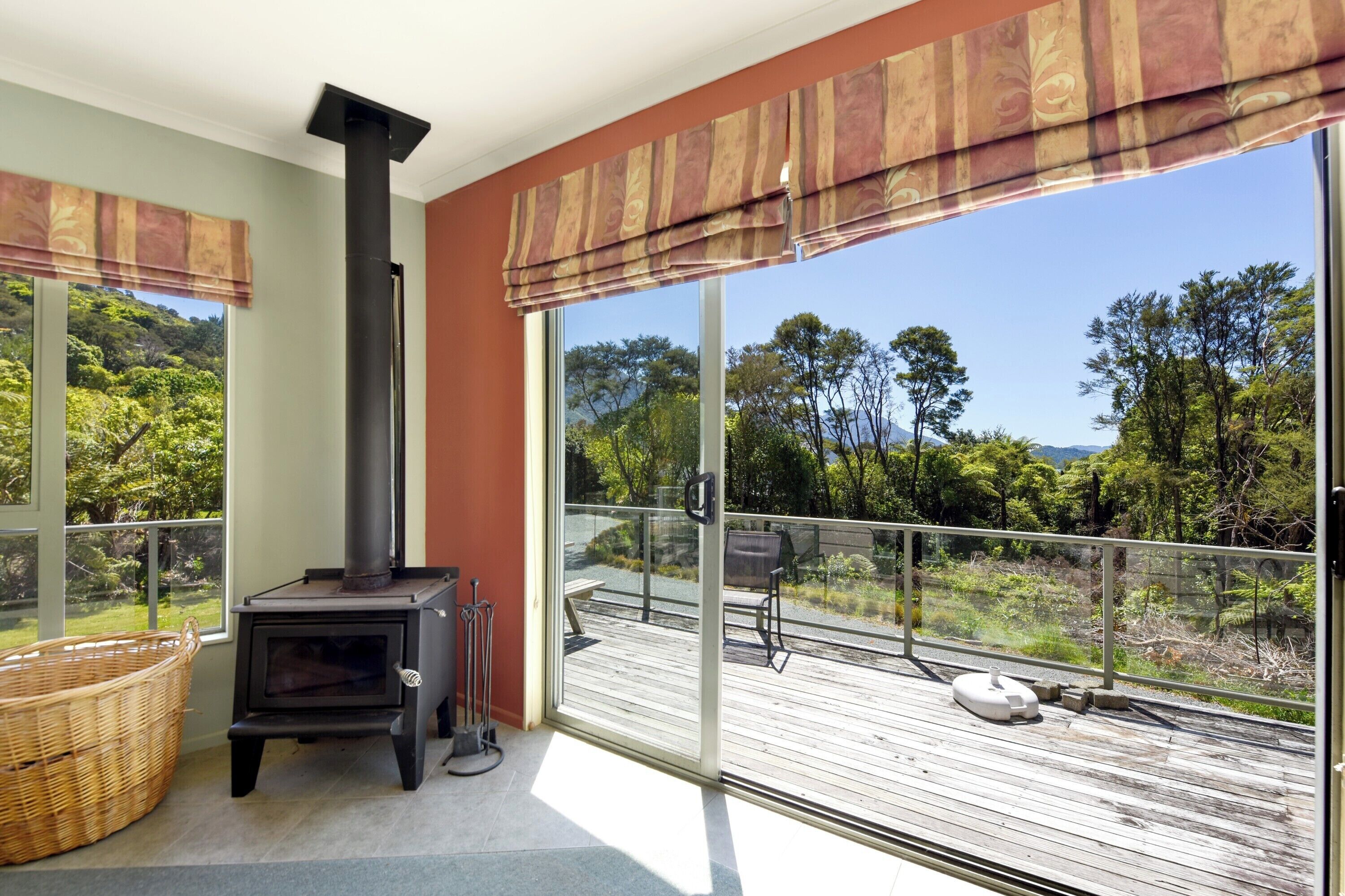 A balcony with a wood-burning stove, a wicker basket, and a view of the surrounding greenery.
