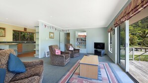A spacious living room with a large window, a flat-screen TV, and a wooden coffee table. - Kereru Retreat at Moetapu Bay (Moetapu Bay)