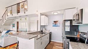 Une cuisine moderne dotée de plans de travail en granit, d’appareils électroménagers en acier inoxydable et d’un escalier menant à l’étage supérieur.