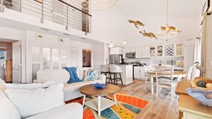 Un vaste espace de vie doté d’un plafond haut, un coin repas avec une table en bois et une cuisine avec des meubles blancs.
