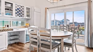 Une cuisine moderne avec des meubles blancs, une table à manger avec des chaises et une vue sur l’extérieur grâce à de grandes fenêtres.
