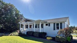 Ein eingeschossiges Haus mit Veranda, einem kleinen Garten und blauem Himmel.