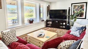 Ein Wohnzimmer mit rotem Sofa, Couchtisch, Fernseher und großen Fenstern.