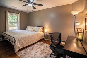 A bedroom with a bed, a desk, a chair, a standing lamp, and a ceiling fan.