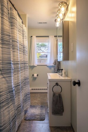 A bathroom with a striped shower curtain, a sink with a towel ring, and a window with a view of the outside.