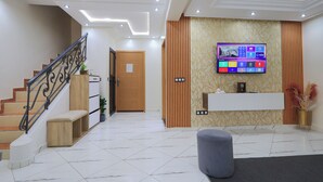 Un vestíbulo moderno con una escalera, un mostrador de recepción y un televisor de pantalla plana montado en la pared.