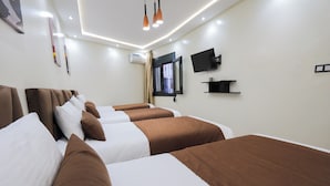 Una habitación de hotel con cuatro camas, un televisor de pantalla plana, una ventana con cortinas y un aire acondicionado instalado.