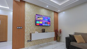 Una sala de estar moderna con un televisor de pantalla plana montado en una pared con diseño, un sofá con cojines y un jarrón decorativo con flores secas.