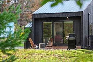 A modern building with a dark exterior, large windows, and a patio area with outdoor furniture. - Loft 4 - Designer Cabin, Walls of Light, Sauna (Brownsville)