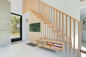 Un interior moderno con una escalera de madera, un televisor de pantalla plana montado en la pared y una estantería empotrada llena de libros.