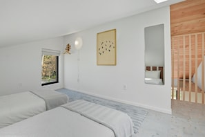 A bedroom with two beds, a window, a wall-mounted light fixture, and a framed picture.