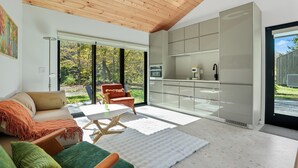 Sala de estar moderna com teto de madeira, um sofá, uma mesa de centro e uma área de cozinha com uma janela ampla.