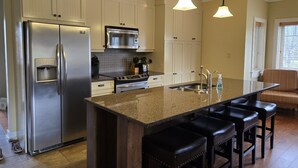 Una cocina moderna con electrodomésticos de acero inoxidable, una isla de granito y taburetes de bar.