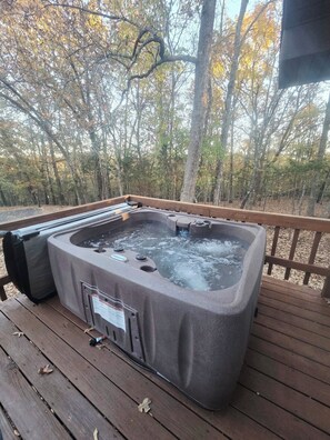 Un jacuzzi en una terraza de madera con vista al bosque.