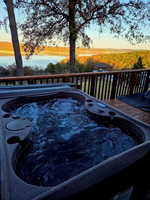 Un bain à remous sur une terrasse en bois, avec vue sur un lac et des arbres.