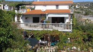 A two-story house with a balcony, surrounded by greenery and a hillside in the background. - Comfort Two Bedroom Apartment with Terrace (Rogoznica)