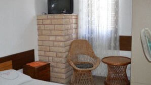 A hotel room with a brick fireplace, a wicker chair, a small round table, and a television on a stand. - Comfort Two Bedroom Apartment with Terrace (Rogoznica)